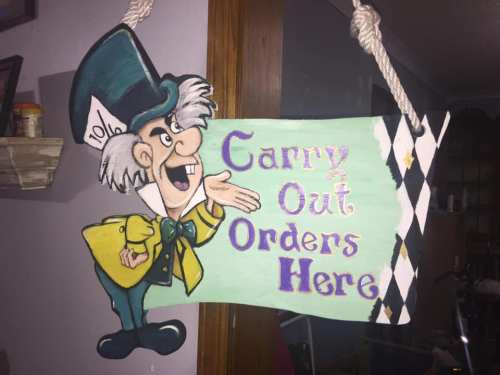 Colorful sign featuring a cartoon character with a top hat, saying "Carry Out Orders Here" in playful lettering.