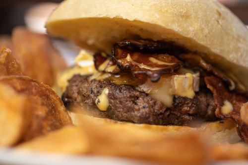 Close-up of a juicy burger with melted cheese and bacon, served with crispy potato chips on the side.