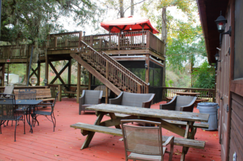 Outdoor deck area with wooden picnic tables, chairs, and a staircase leading to a shaded upper level with a red umbrella.