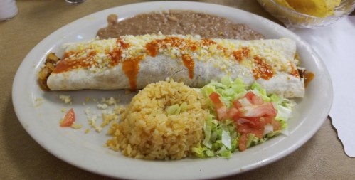 A plate featuring a large burrito topped with cheese and sauce, served with rice, refried beans, and a side salad.