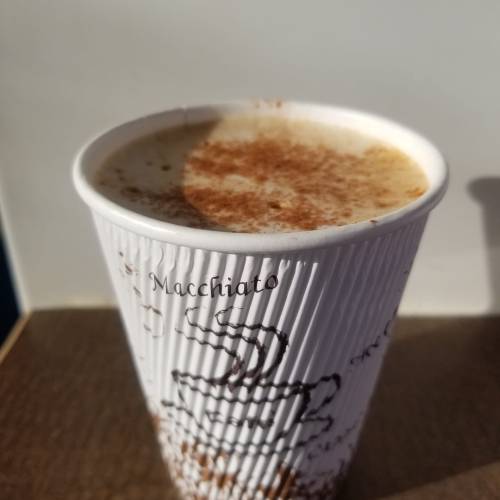 A close-up of a macchiato in a paper cup, topped with a sprinkle of cinnamon.