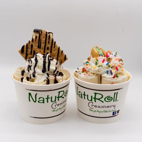 Two cups of ice cream topped with whipped cream, sprinkles, chocolate drizzle, and a graham cracker.