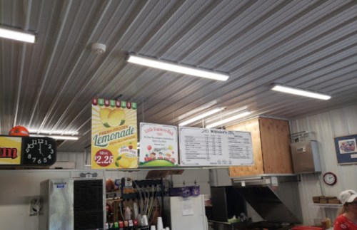 Interior of a food stand with a menu board, lemonade sign, and kitchen equipment visible under bright overhead lights.