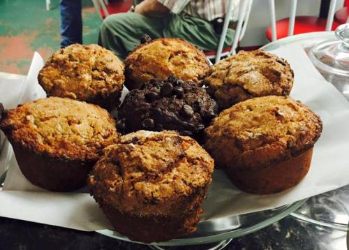 A platter of freshly baked muffins, including chocolate chip and assorted flavors, arranged on a white paper.