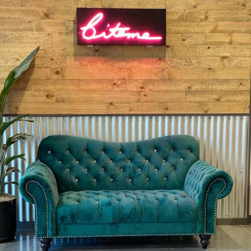 A teal tufted couch sits against a wooden wall, with a neon sign above that reads "bitome."