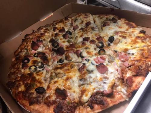 A freshly baked pizza with various toppings, including cheese, pepperoni, olives, and ham, in a pizza box.