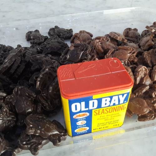 A container of Old Bay seasoning surrounded by chocolate crab-shaped candies on a clear surface.
