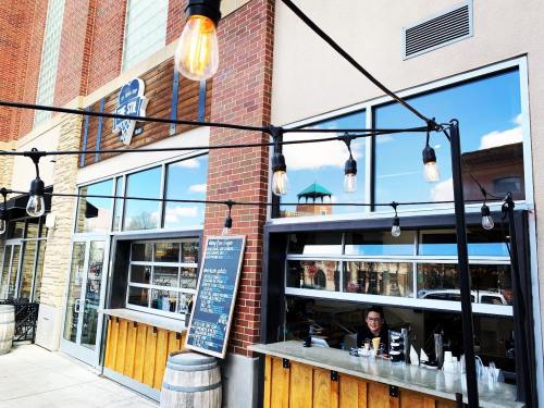A woman serves customers at a window of a brick building with string lights and a menu board outside.