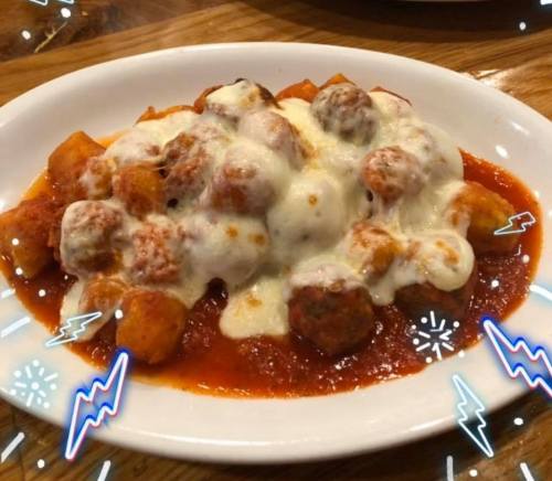 A plate of gnocchi topped with meatballs and melted cheese in a rich tomato sauce.