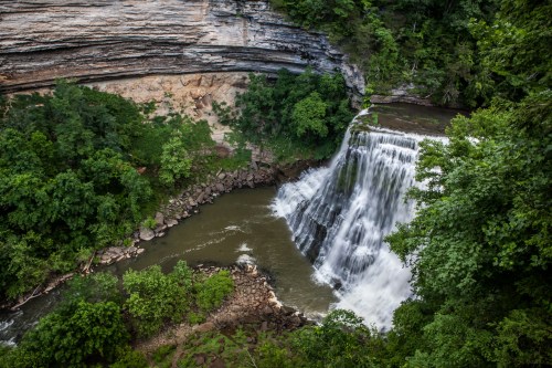 A cascading waterfall surrounded by lush greenery and rocky cliffs, flowing into a serene river below.