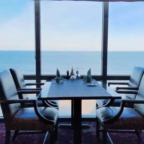 A dining table set for two by a large window overlooking the ocean.