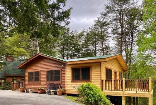 A wooden cabin with a deck, surrounded by trees, on a cloudy day. Potted plants decorate the entrance.