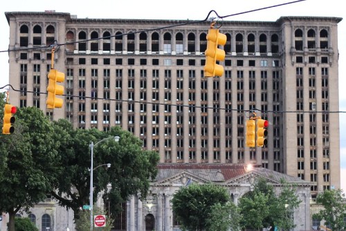 Abandoned building with a large facade, surrounded by traffic lights and trees, showcasing urban decay.