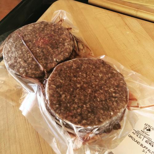 Two vacuum-sealed ground buffalo patties on a wooden surface.