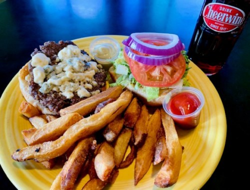 A plate with a burger topped with lettuce, tomato, onion, and blue cheese, served with fries and a Cheerwine soda.