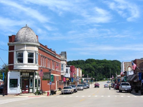 A small town street lined with historic buildings and American flags, under a blue sky with scattered clouds.