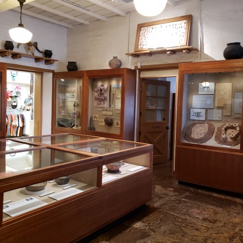 Interior of a museum exhibit featuring display cases with artifacts and informational panels, warmly lit and inviting.