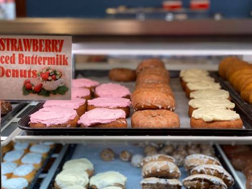 A display of assorted donuts, including strawberry and buttermilk varieties, with pink and yellow frosting.