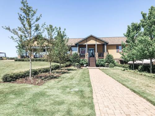 A pathway leads to a yellow house surrounded by green trees and well-maintained landscaping under a clear blue sky.