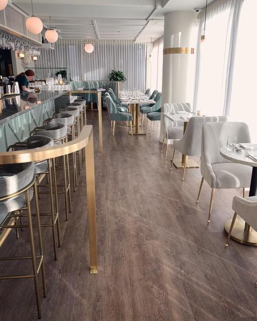 Modern restaurant interior featuring a bar, elegant seating, and large windows with natural light.