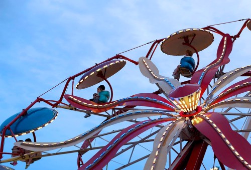 A colorful amusement ride with two people seated in gondolas against a blue sky.