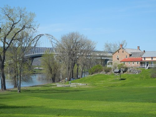A scenic view of a river, a bridge in the background, and a historic house surrounded by green grass and trees.