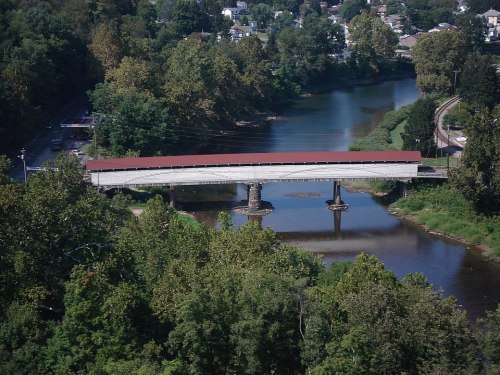 Aerial view of a covered bridge spanning a river, surrounded by lush greenery and trees.
