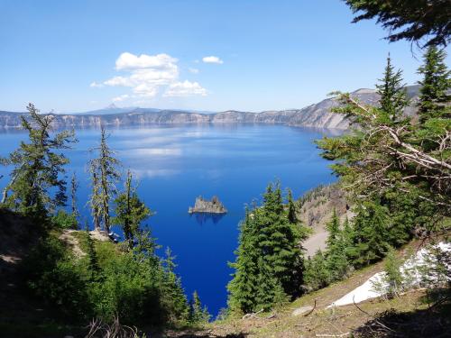 A serene view of a blue lake surrounded by trees and mountains, featuring a small island in the center.