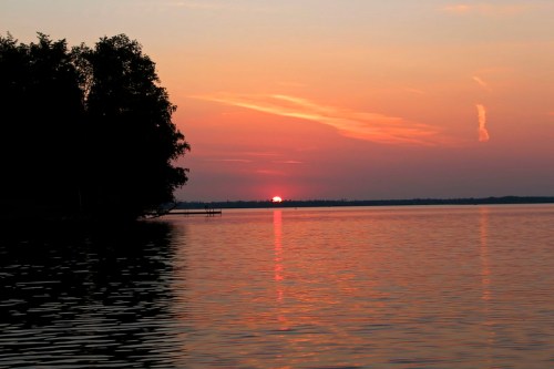 A serene sunset over a calm lake, with vibrant orange and pink hues reflecting on the water's surface.