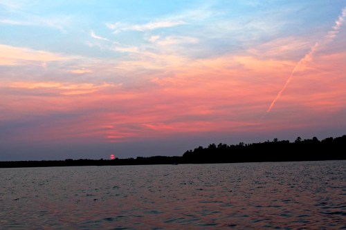 A serene sunset over a calm lake, with vibrant pink and blue hues in the sky and silhouettes of trees on the horizon.