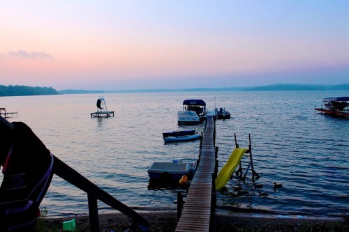 A serene lake at dusk with boats docked and a wooden pier extending into the water, surrounded by soft pastel skies.