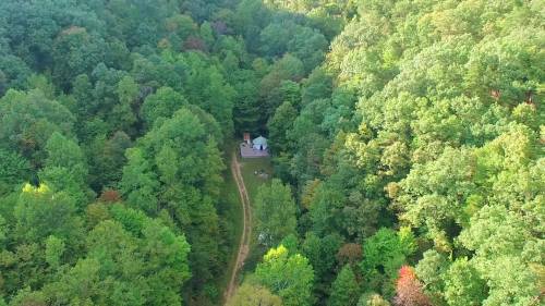 Aerial view of a small cabin surrounded by dense green forest and a winding dirt path.