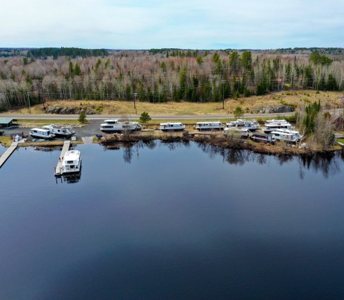 Aerial view of a calm lake with several boats docked along the shore and trees in the background.