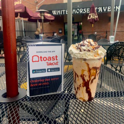 A dessert drink topped with whipped cream and chocolate drizzle next to a sign promoting the Toast TakeOut app.