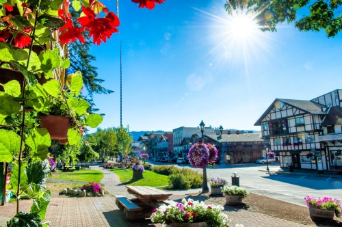 A sunny street scene with vibrant flowers, benches, and charming buildings in a picturesque town.