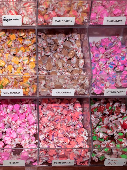 A display of colorful candies in clear bins, labeled with flavors like peppermint, chocolate, and cotton candy.