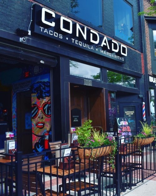 Exterior of Condado restaurant featuring a vibrant sign and outdoor seating with colorful planters.