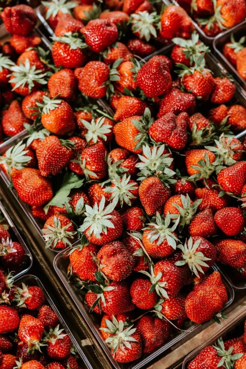 A close-up of fresh, vibrant strawberries piled in containers, showcasing their bright red color and green leaves.