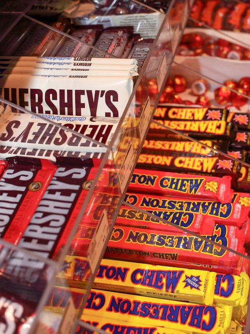 A display of various candy bars, including Hershey's and Charleston Chew, arranged in clear containers.