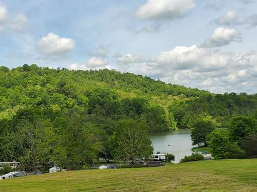 A serene lake surrounded by lush green hills and trees under a partly cloudy sky.