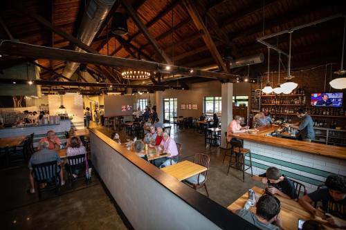 A spacious restaurant interior with wooden beams, patrons dining at tables, and a bar area with people enjoying drinks.