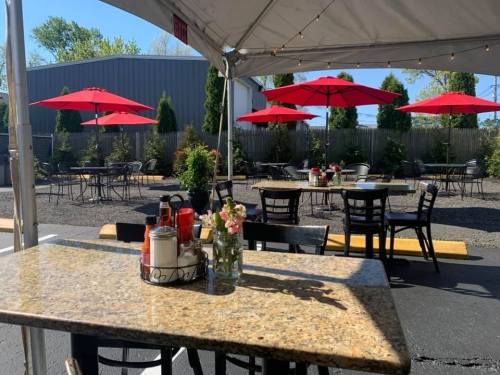 Outdoor dining area with red umbrellas, tables, and a granite table featuring condiments and a flower vase.