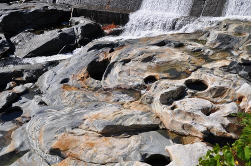 Smooth, multicolored rocks with natural holes, beside a flowing waterfall and lush greenery.