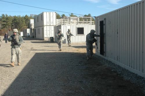 Soldiers in military gear maneuvering around container-like structures during a training exercise.
