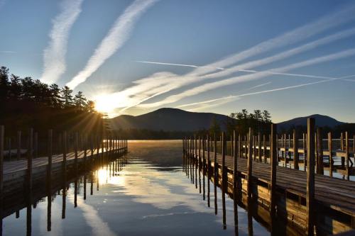 Sunrise over a calm lake, with wooden docks extending into the water and mountains in the background, streaked clouds above.