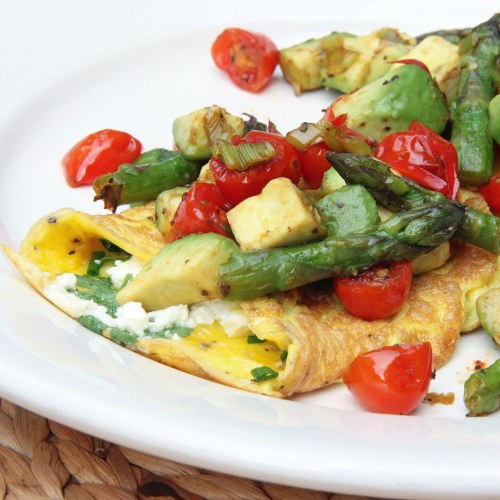 A colorful omelette topped with sautéed asparagus, cherry tomatoes, and diced zucchini on a white plate.