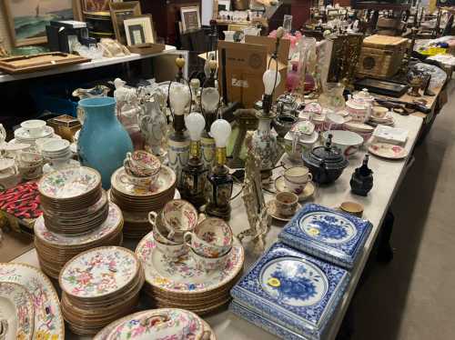 A variety of vintage items including plates, teacups, lamps, and decorative pieces displayed on a table.