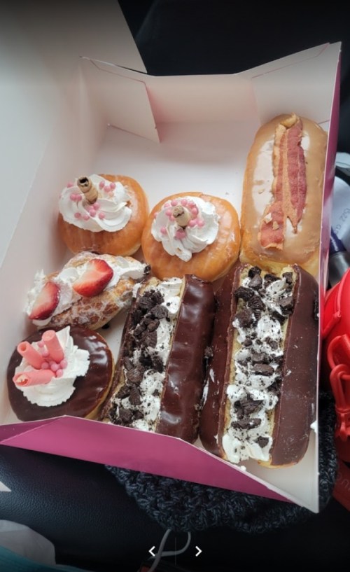 A box of assorted donuts, including cream-filled, topped with chocolate, strawberries, and sprinkles.