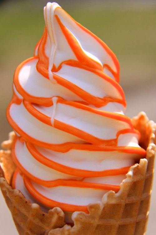 A close-up of a soft-serve ice cream cone with orange swirls on top of creamy white ice cream.