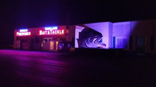 A brightly lit bait and tackle shop at night, featuring a large fish sculpture outside.